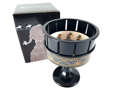 Praxinoskopas juodas ant kojelės su auksiniu ornamentu, viršaus kampo kadras rodo besisukančias lėles ir pakuotę fone