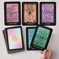 tarot kortos su pasteliniais nugarėliais ir žalia Four of Pentacles korta rankoje, matomi kiti dizaino variantai