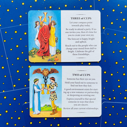 tarot kortos Rider–Waite stiliaus: dvi kortos (Three of Cups ir Two of Cups) ant mėlyno žvaigždėto fono, aiškinimo tekstai matomi