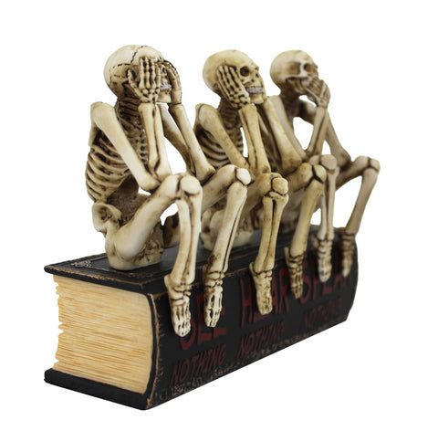 Skeletų figūrėlė, trys senoviniai kaulai sėdi ant juodos knygos kaip Helovino dekoracija, kiekvienos rankos poza skiriasi