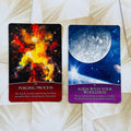 Orakulų kortos: dvi kortos šone — raudona "Purging Process" su ugnine grafika ir mėlyna "Align With Your Wholeness" su mėnuliu