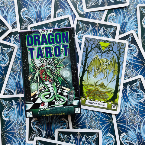 Dragon Tarot kortų rinkinys su žalios dėžutės dizainu ir atversta Page of Coins korta ant mėlynos nugarėlių kompozicijos