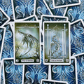 Tarot kortos su žaliai mėlynu drakono dizainu, dvi atverstos kortos (Page of Swords ir Four of Swords) plokščiai išdėstytos