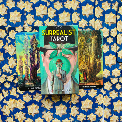 Surrealist Tarot kortos Luigi Di Giammarino dėžutė centre, dvi kortos šone ant mėlyno geometrinio fono