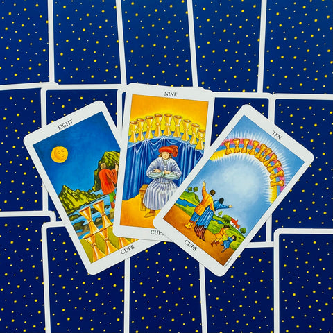 tarot kortos Rider‑Waite stiliaus, žvaigždėtu mėlynu užpakaliu, atvertos 8, 9 ir 10 taurės centriniam taro skaitymui