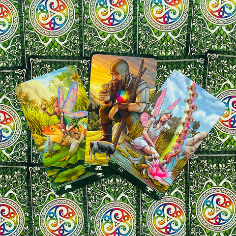 Tarot kortos su ryškiomis fėjų iliustracijomis, trijų kortų fanuotas vaizdas ir žalios ornamentuotos nugarėlės