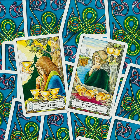 Tarot kortos su atverstomis Keturių ir Penkių taurų kortomis, aiškiai matomomis spalvotais keltų raštais gale.