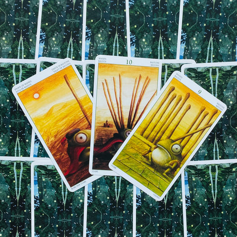 Tarot kortos — trys geltoni Lazdų rūšies kortos (9, 10 ir riteris) iš iliustruotos kaladės ant žvaigždėto žalio nugarėlių fono