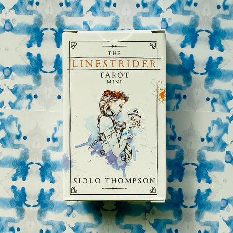 Mini tarot kortos Linestrider — baltas mažų gabaritų dėklas su akvareline moters iliustracija ir autoriaus Siolo Thompson užrašu