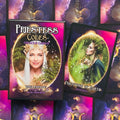Priestess Codes oracle kortos – violetinė dėžutė su elfiška panelė priekinėje pusėje ir atversta „Priestess of Earth“ korta