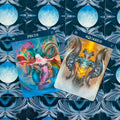 tarot kortos „Žuvys“ ir „Vandenis“ su ryškiomis fantazijos iliustracijomis ant mėlynos mėnulio nugarėlės, iš viršaus pasuktos kampu
