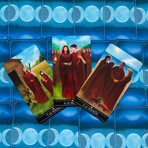 Tarot kortos — trijų kortų išklotinė (5, 6, 7 lazdų), atviros figūrų iliustracijos ant mėlyno mėnulio fono