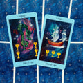 tarot kortos mėlynu rėmeliu, dvi atverstos kortos (Four of Cups ir Three of Cups) ant žvaigždėto mėlyno audinio
