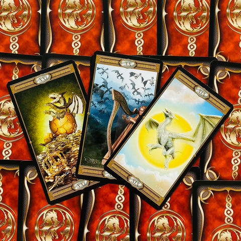 Tarot kortos drakonų tematikos — trys atidengtos kortos: mažas drakonas ant lobio, harfa ir baltas drakonas, raudonos ornamentuotos nugarėlės
