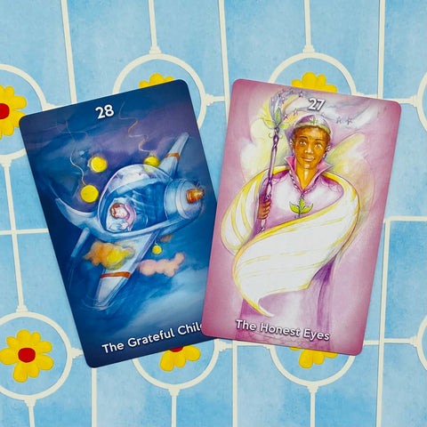 Orakulo kortos: dvi atviros versijos — mėlyna The Grateful Child ir rožinė The Honest Eyes, iš viršaus ant mėlyno gėlių fono