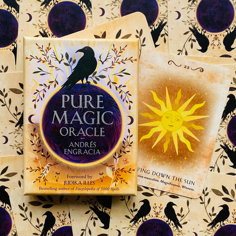 Pure Magic Oracle kortų rinkinys su dėklu ir atvira saulės korta, Andrés Engracia dizainas, kremine‑auksine palete ir varnėno motyvu fone
