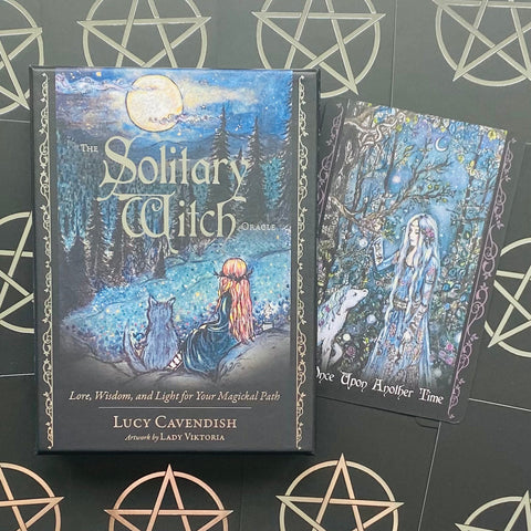 Orakulo kortos The Solitary Witch dėžutėje su mėlynu mėnulio viršeliu, šone viena atversta korta su moters iliustracija ir Lucy Cavendish autorystės ženklu