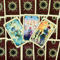tarot kortos su ryškiomis fantazijos iliustracijomis — trys atverstos kortos pastelinių tonų, raudonos rombinės nugarėlės