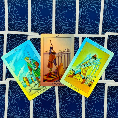 Tarot kortos Rider–Waite: trys kardų kortos išskleistos fanu, matomi 5, 6 ir 7 variantai ant mėlyno nugarėlių fono