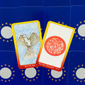 Tarot kortos, dvi fronte atidengtos: Ace of Air su balandžiu ir The Fire Element su raudonu ornamentu, geltoni rėmai ant mėlyno fono