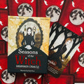 Kortų rinkinys Seasons of the Witch Samhain Oracle: dėžutės priekinis dangtis ir viena atversta korta su juodos suknios moterimi ant raudono mėnulio fono