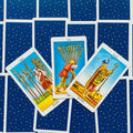 Tarot kortos Rider–Waite stiliaus, trys lazdų kortos centre (Nine, Ten, Page), išdėstytos ant mėlyno žvaigždėto fono