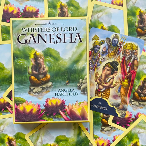Ganesha kortos Whispers of Lord Ganesha – ryškiai geltonu borteliu dėžutė ir atversta korta „Guidance“ su rožiniais lotosais, rodoma iš viršaus