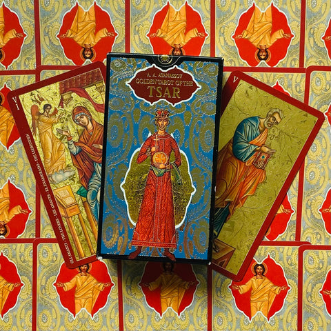 Tarot kortos dėžutė "Golden Tarot of the Tsar" centre su dviem atverstomis kortomis kampuose ant ornamentuoto raudono fono