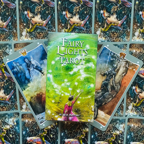 Fairy Lights Tarot kortos, žalia dėžutė su spiraliniu raštu padėta ant atvertų iliustruotų kortų fone, aut. Lucia Mattioli