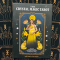 Priekinis The Crystal Magic Tarot denio juodos pakuotės vaizdas su geltonomis moters ir kačių iliustracijomis, arti centro, išsiskiria dekoratyviu fonu