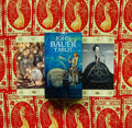 John Bauer tarot dėžutė mėlynu viršeliu centre ant raštuoto raudono fono, šalia atvertos 9 ir 10 kortos