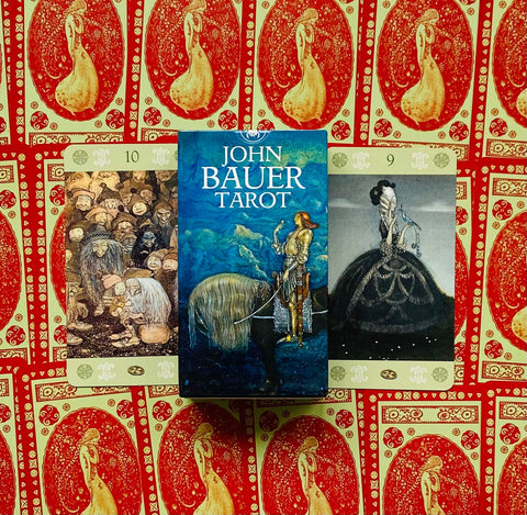 John Bauer tarot dėžutė mėlynu viršeliu centre ant raštuoto raudono fono, šalia atvertos 9 ir 10 kortos