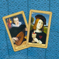 Tarot kortos su Renesanso paveikslų dizainu, dvi kortos (Knight of Cups ir Page of Cups) ant mėlyno raštuoto fono, fotografuotos iš viršaus