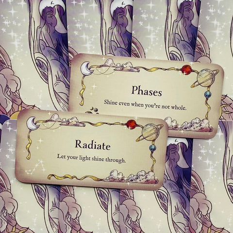 Įkvėpimo kortelės – dvi kreminės kortelės su planetų rėmeliais ir tekstais Radiate ir Phases, rodoma pavyzdinė žinutė ir dizainas