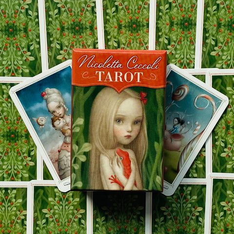 Tarot kortos Nicoletta Ceccoli – raudona dėžutė su mergaitės iliustracija, išskleistos kortos ir žalias augalinis fonas