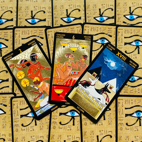 Tarot kortos su auksuotu Egipto dizainu, trys atverstos kortos fanuotos ant dėklo su ryškiomis mėlynomis akimis
