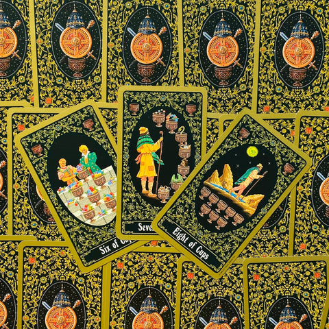 Tarot kortos juodu fono ir auksiniu ornamentu, atviros trys taurės — šešių, septynių ir aštuonių taurių kortos, pasvirusios viena ant kitos