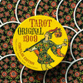 tarot kortos Original 1909 apvalioje geltonoje dėžutėje su klajūno iliustracija, matomi juodi gėlių rašto kortų nugarėlės