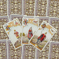 Tarot kortos vintage leidimas — trys atverstos figūrinės kortos ant ornamentuotos violetinės nugarėlės