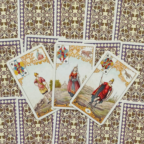 Tarot kortos vintage leidimas — trys atverstos figūrinės kortos ant ornamentuotos violetinės nugarėlės
