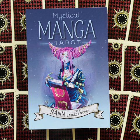 Manga tarot kortos: purpurinė‑mėlyna dėžutė su rožiniais plaukais personažu, autorius Rann, padėtos ant raštuotų kortų