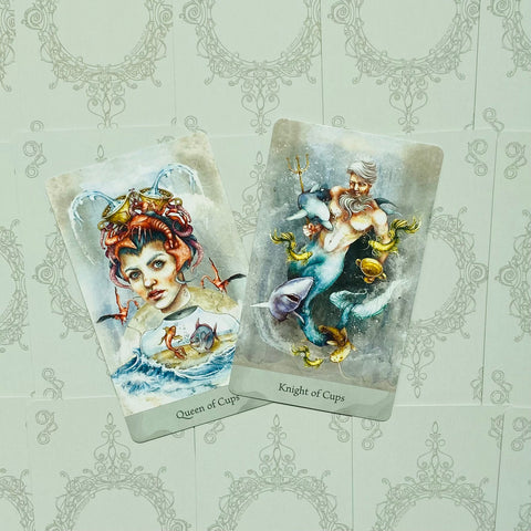 Tarot kortos su Queen of Cups ir Knight of Cups iliustracijomis, pastelinės spalvos, atvertos priešais ornamentinį foną