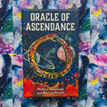 Oracle of Ascendance kortų kaladė – juoda dėžutė su spalvotu uroboru, planetų iliustracija ir autoriais ant priekinio dangčio