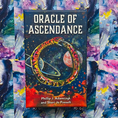 Oracle of Ascendance kortų kaladė – juoda dėžutė su spalvotu uroboru, planetų iliustracija ir autoriais ant priekinio dangčio
