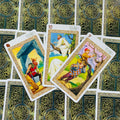 Tarot kortos su keltišku žaliu nugarėlių raštu, trys atverstos iliustruotos priekio kortos parodytos iš viršaus