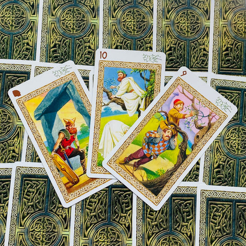 Tarot kortos su keltišku žaliu nugarėlių raštu, trys atverstos iliustruotos priekio kortos parodytos iš viršaus