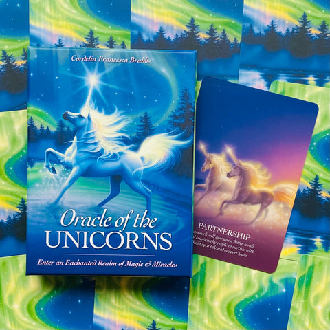 Oracle of the Unicorns kortų rinkinys mėlyname dėkle su atversta „Partnership“ korta ant švytinčios auroros fono