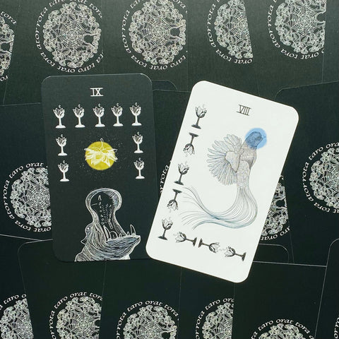 tarot kortos Orat Taro, dvi atverstos kortos: juoda su geltonu žiedu ir balta su mėlynu paukščiu