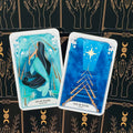 Tarot kortos Aquamarine ir Azurite: Dešimtukas ir Devintukas jūros mėlynomis iliustracijomis ant juodo dėklo su aukso raštais