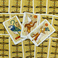 Tarot kortos Egipto motyvais, aukso ir smėlio atspalvių papiruso nugarėlės, trys kortos atvertos ir išdėstytos virš užverstų kortų